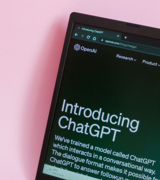 Close-up of a laptop with ChatGPT introduction on screen against a pink background.
